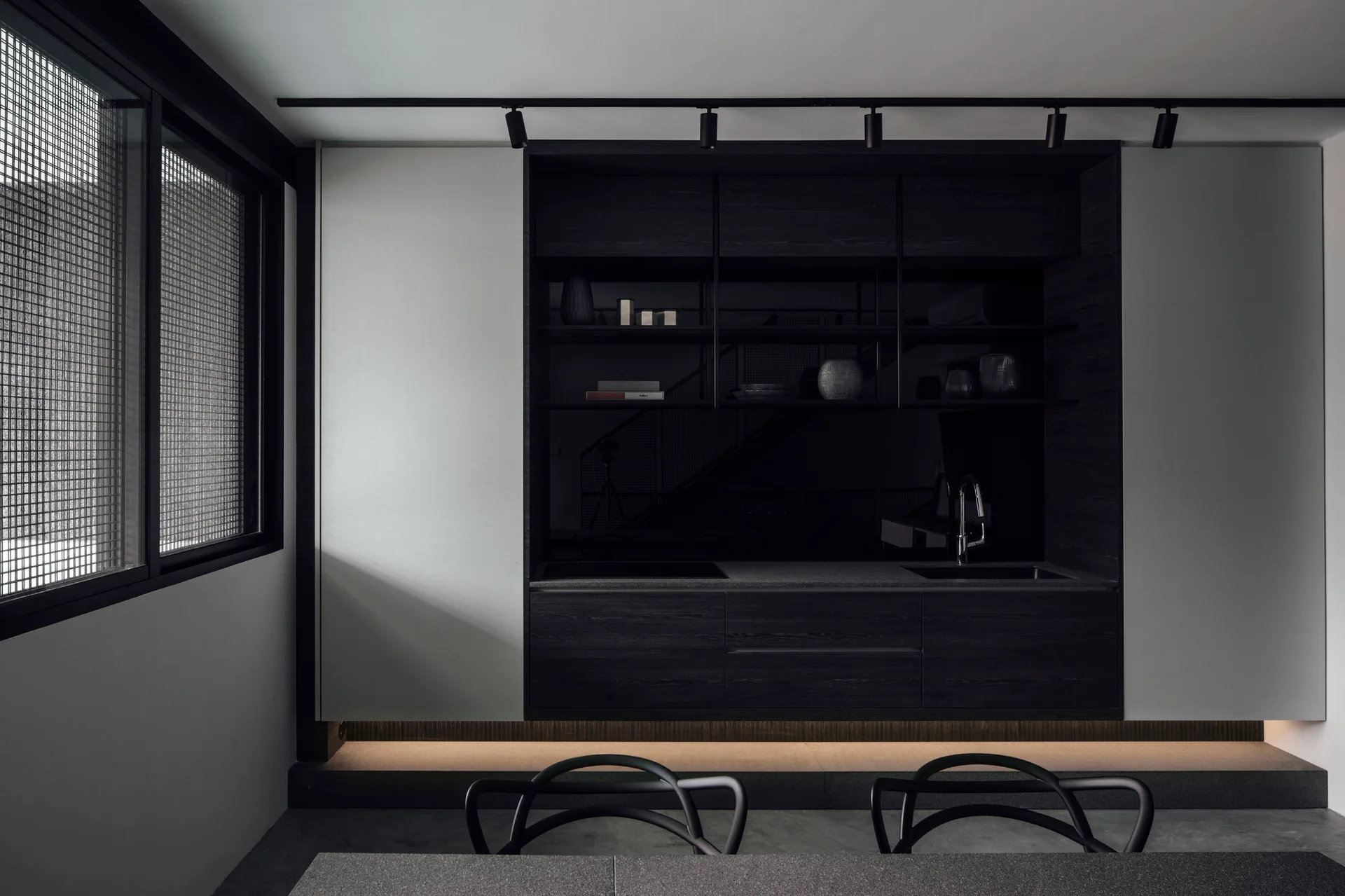 Minimalist dark wood kitchen cabinetry built into a white wall features open shelving, track lighting, and a glowing lower light strip.