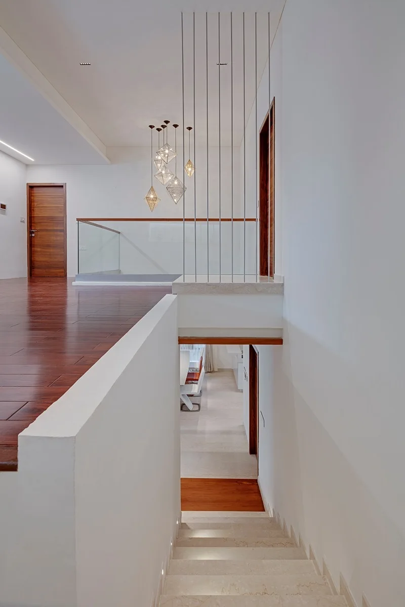 A modern interior staircase features white walls, light stone steps, polished wood floors, and thin vertical metal rod railings.