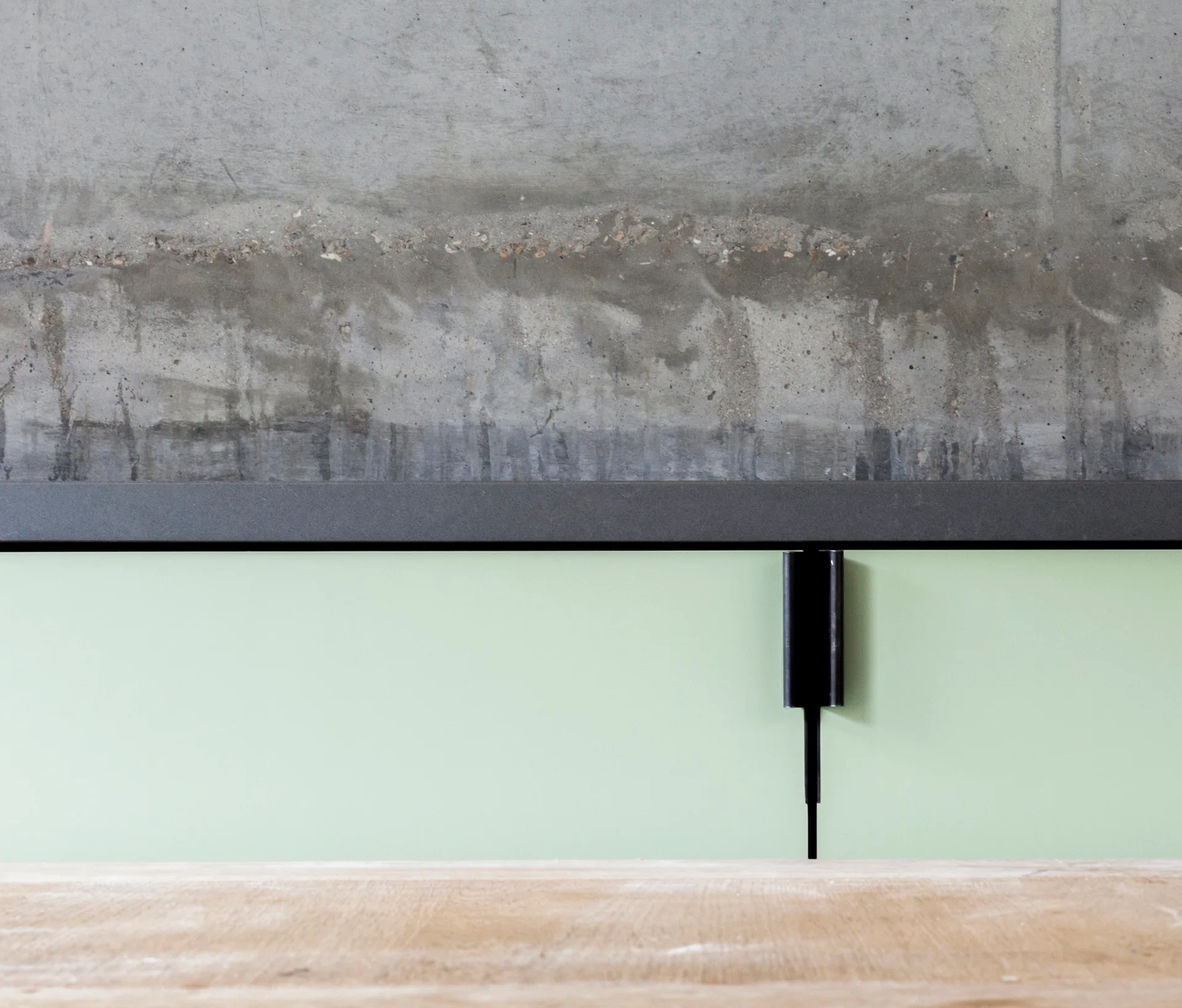 A black metal trim separates a textured grey concrete upper wall from a smooth light green lower wall featuring a black vertical light fixture.