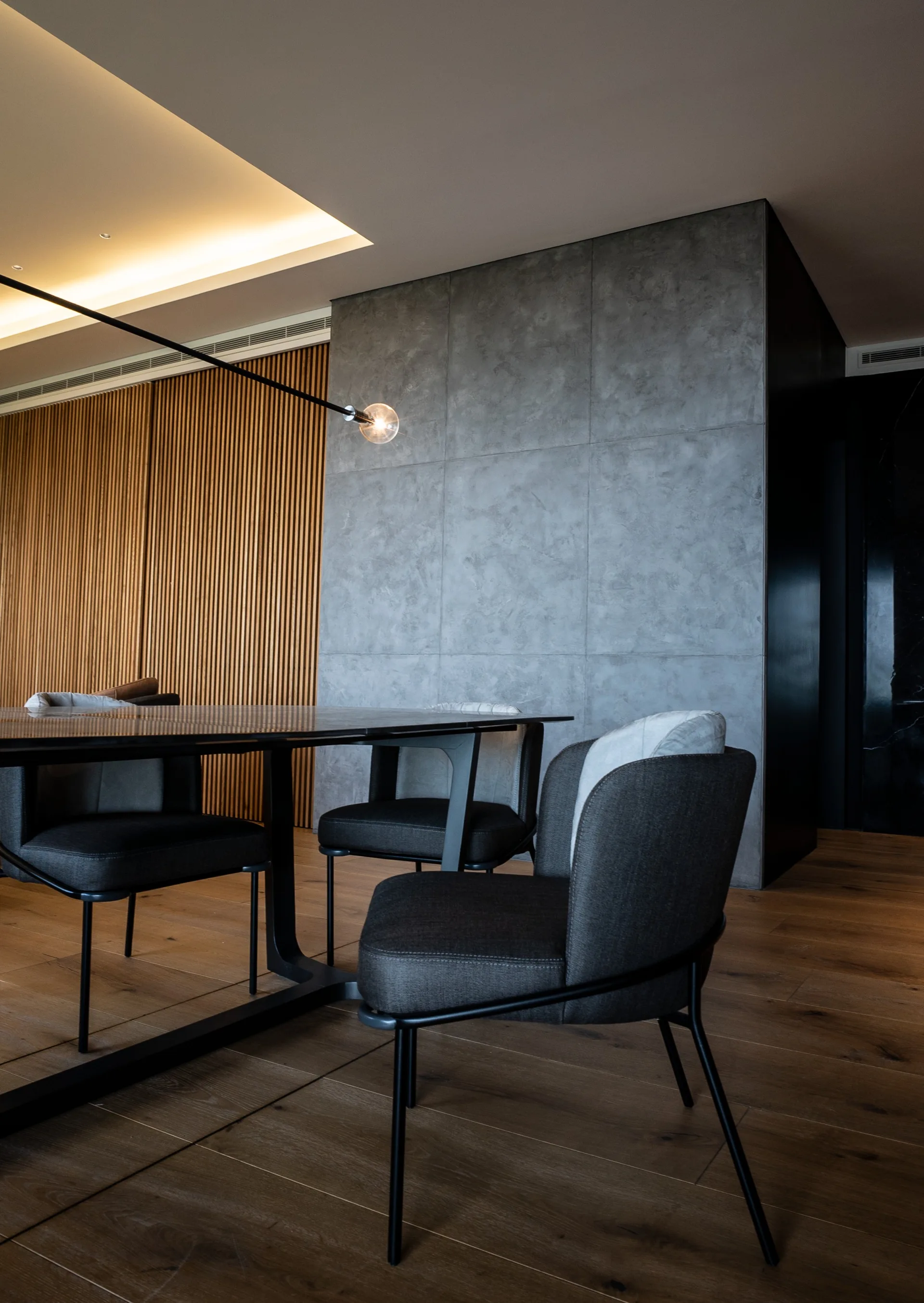 A modern dining room features charcoal upholstered chairs around a dark table set against a textured grey wall and a vertical wood slat partition.