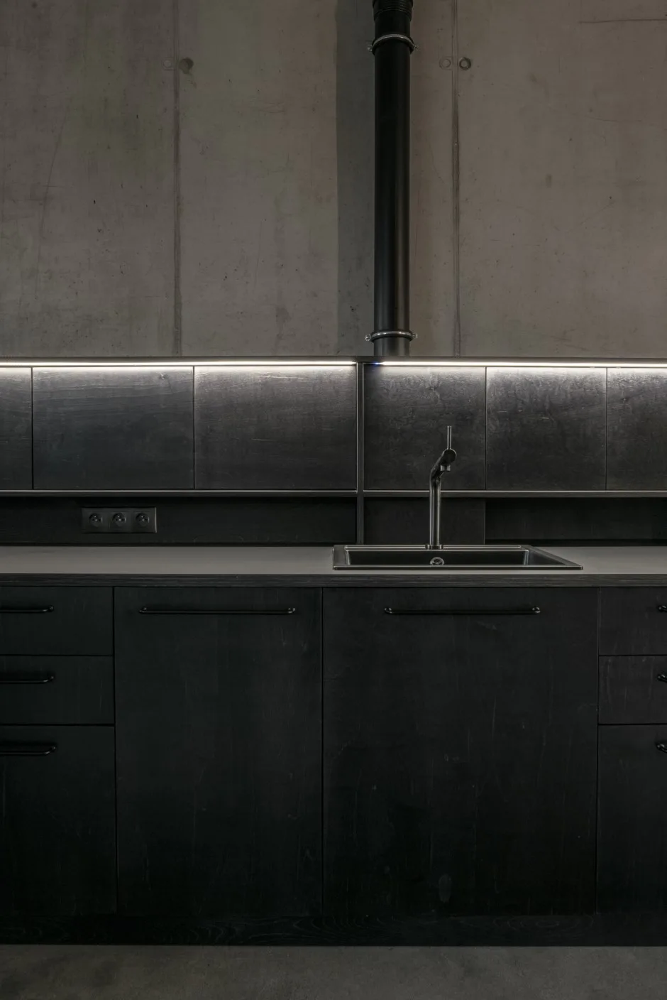 Minimalist dark grey and black kitchen featuring stained wood cabinets, a concrete wall, and an integrated LED strip under a shelf.