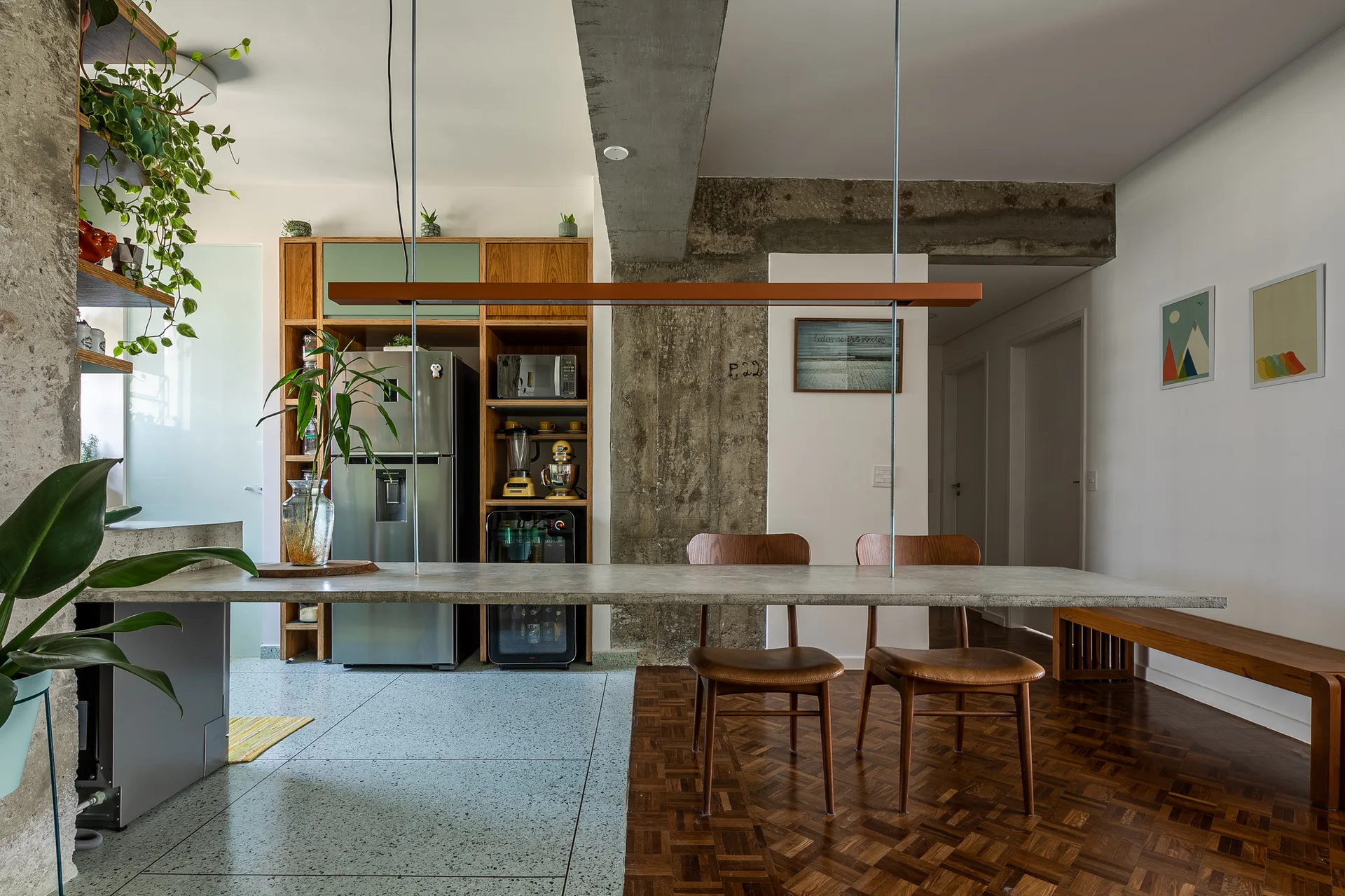 An industrial kitchen features a suspended concrete dining counter positioned over terrazzo tile and warm parquet wood flooring.