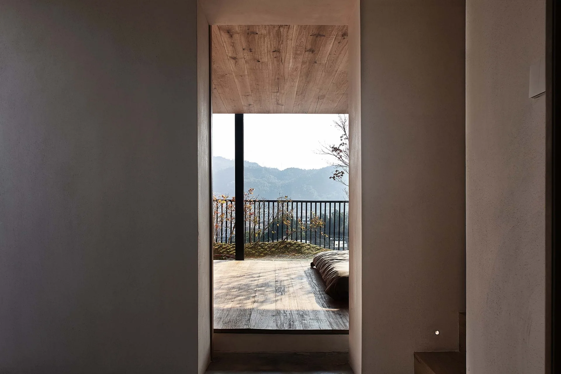 A minimalist plaster archway frames a view of a wooden terrace and distant mountains.