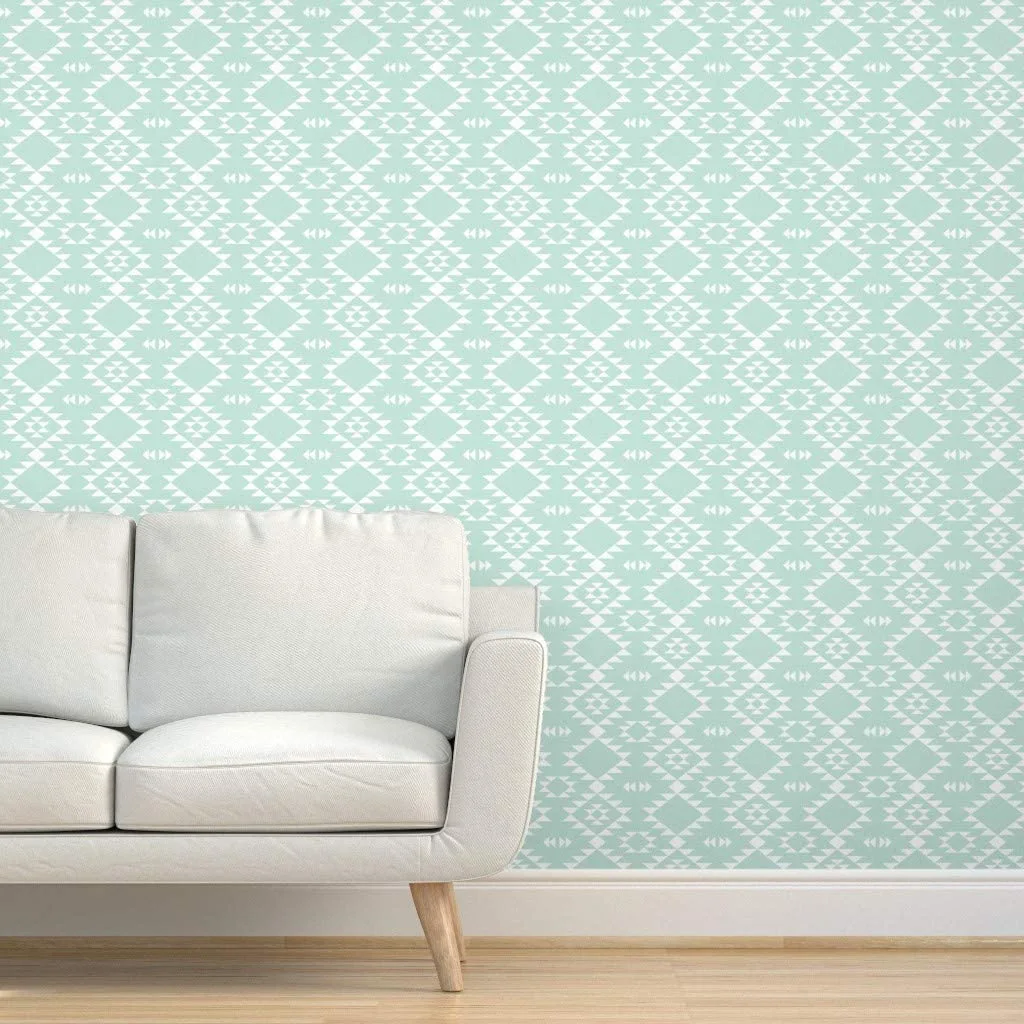 A white modern upholstered sofa stands against a wall covered in a light mint green and white geometric patterned wallpaper above a light wood floor.