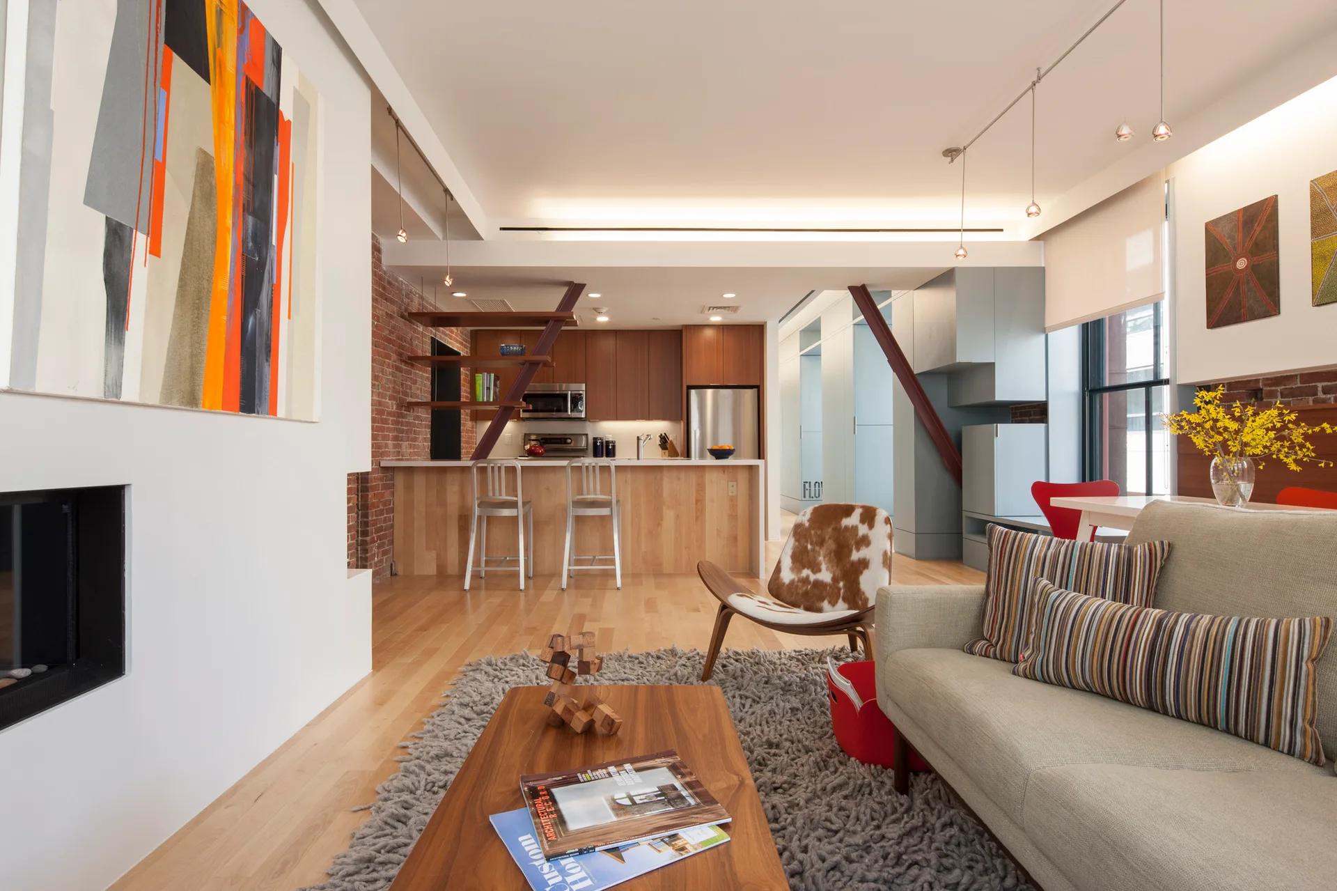 A light-filled open-plan living room with a gray sofa, a shaggy gray rug, a recessed fireplace, and a wood-accented kitchen in the background.