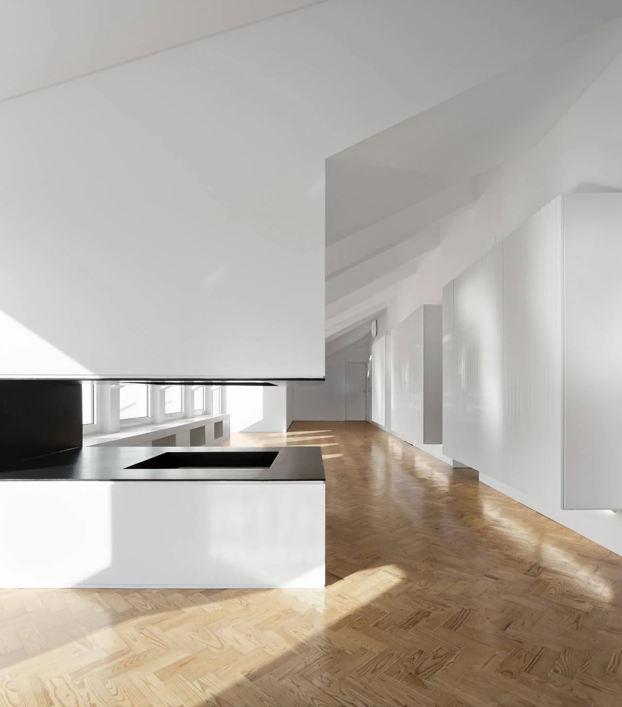 A bright minimalist room features natural light wood herringbone flooring, white built-in wall cabinets, and a modern black and white fireplace.