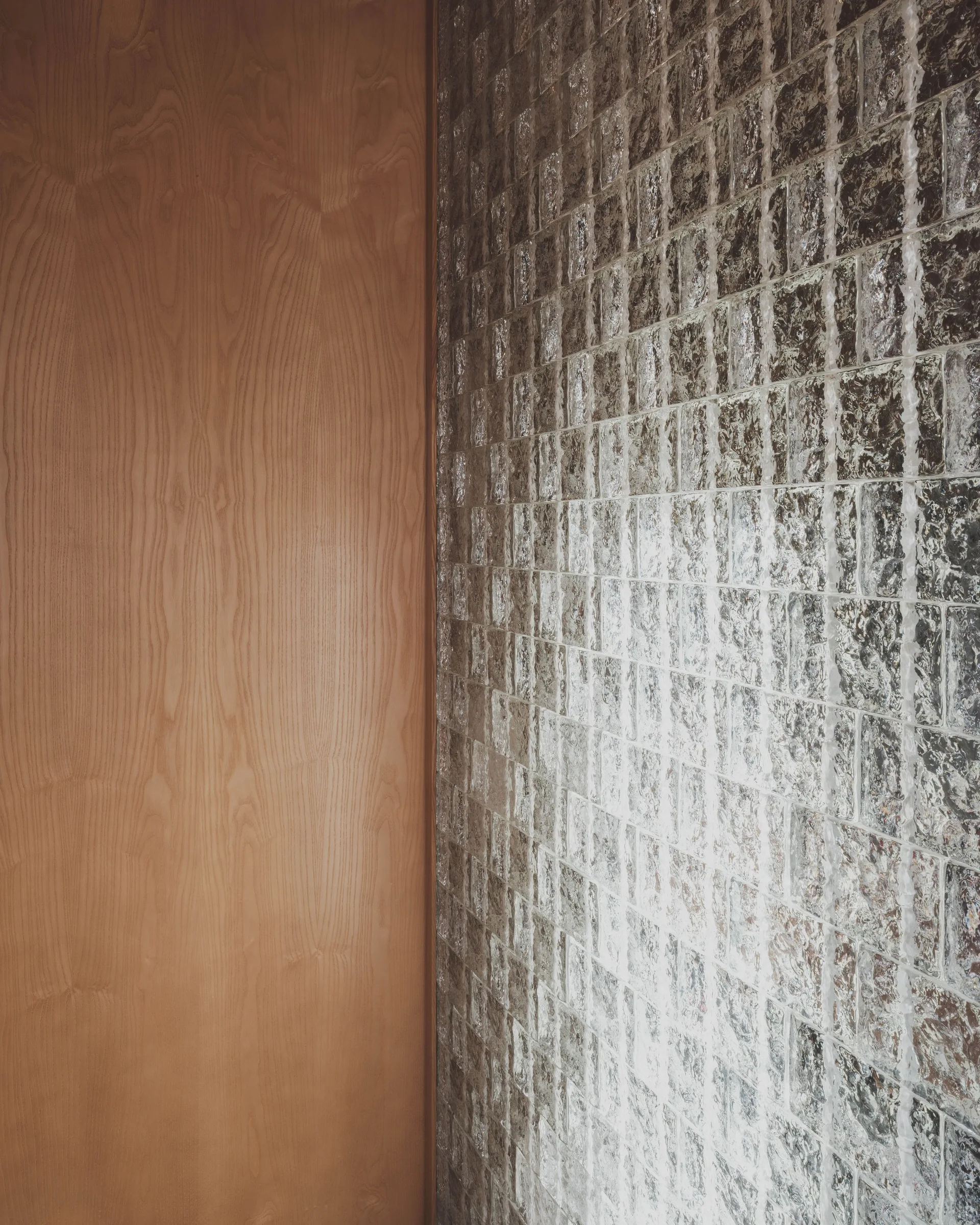 An interior wall showcasing smooth vertical wood paneling adjacent to a textured translucent square glass tile grid.