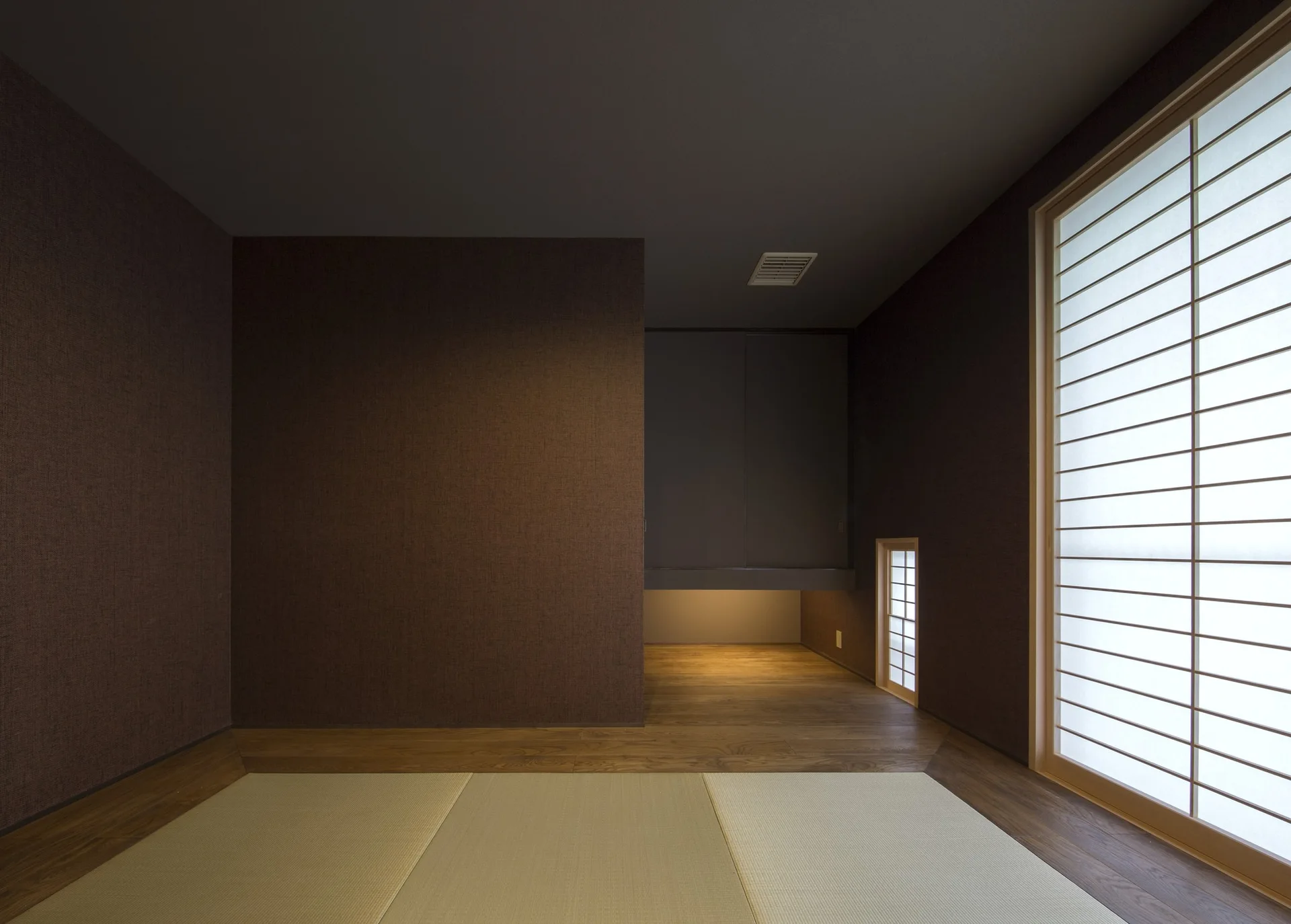 A minimalist Japanese-style room featuring dark brown textured walls, pale woven tatami floor mats, and a large sliding shoji paper screen.