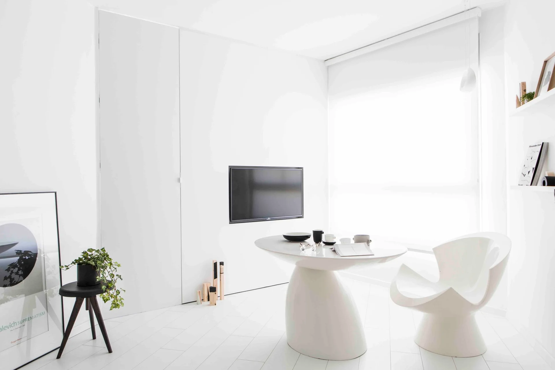 A minimalist white dining room features a glossy white pedestal table, a sculptural white chair, and flush white wall cabinets.