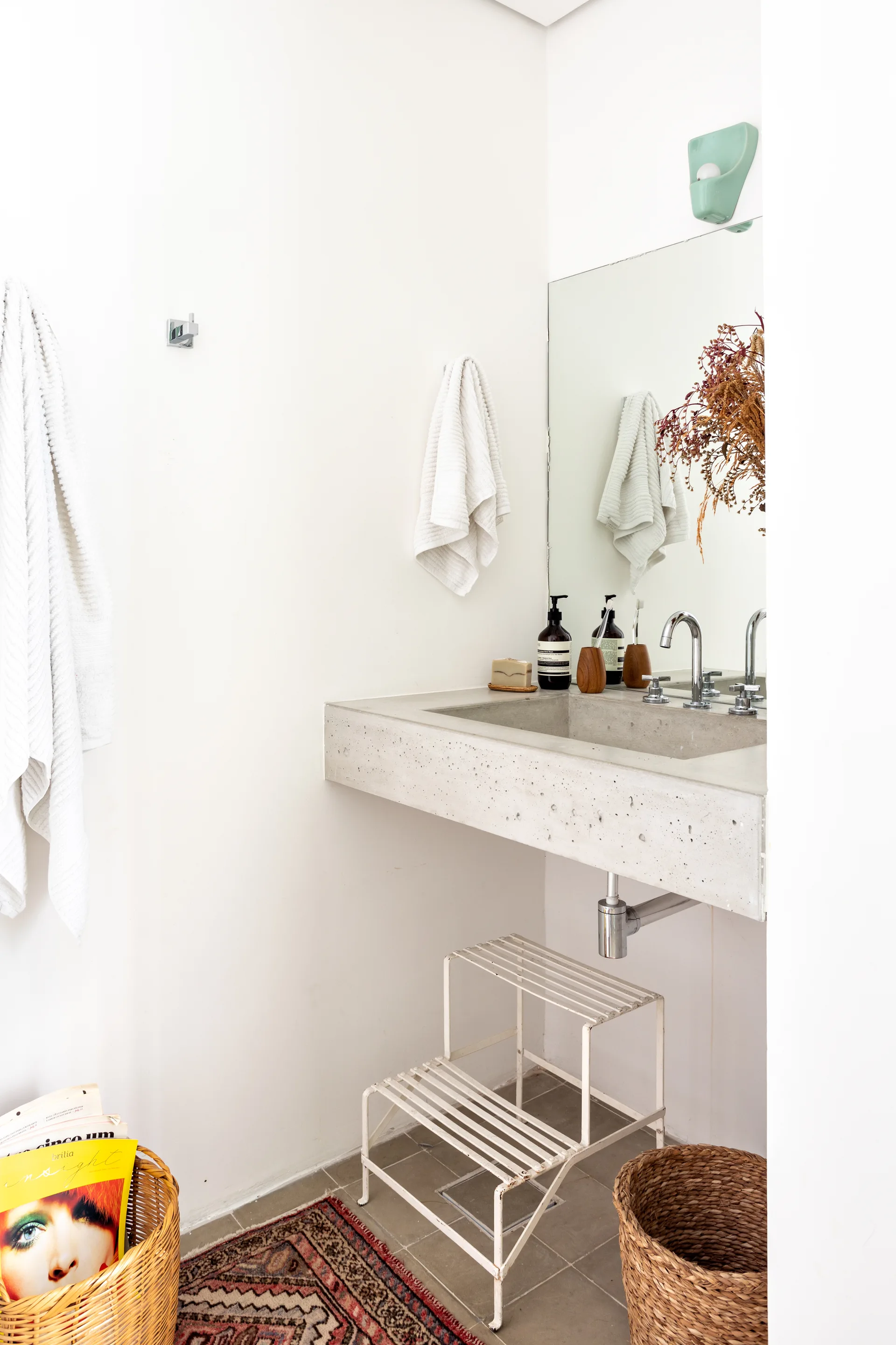 A bathroom featuring a wall-mounted concrete sink, a frameless mirror, white walls, and a white metal step stool on a tiled floor.