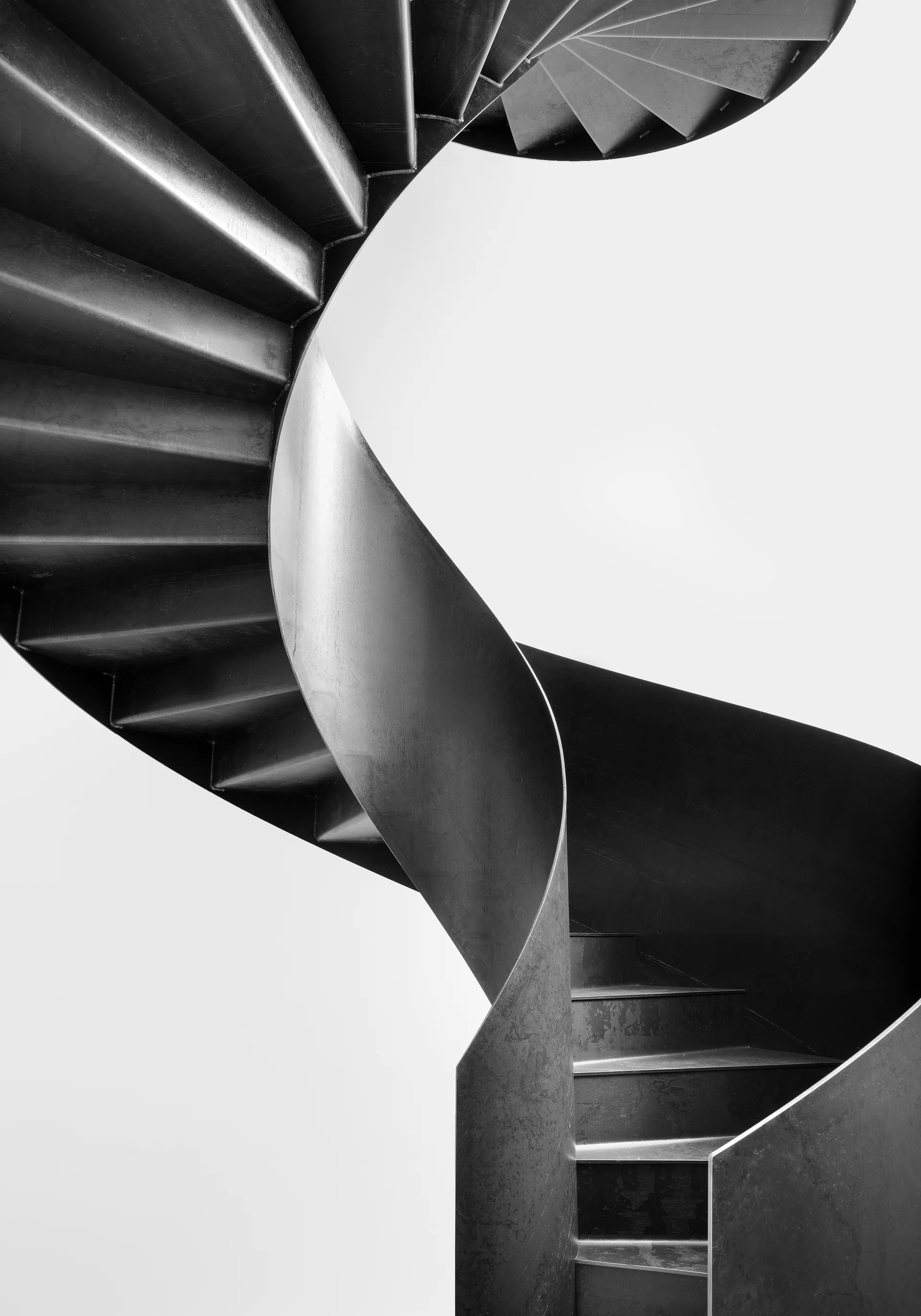A black and white close-up of a modern helical spiral staircase constructed of dark metal with smooth solid railings against a plain white background.