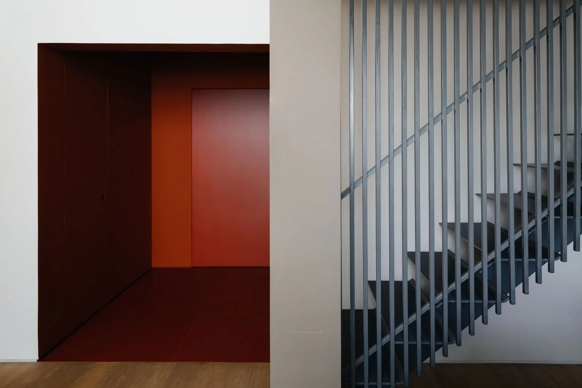 A minimalist interior featuring a modern metal staircase with vertical balusters next to a recessed entryway painted entirely in deep red.