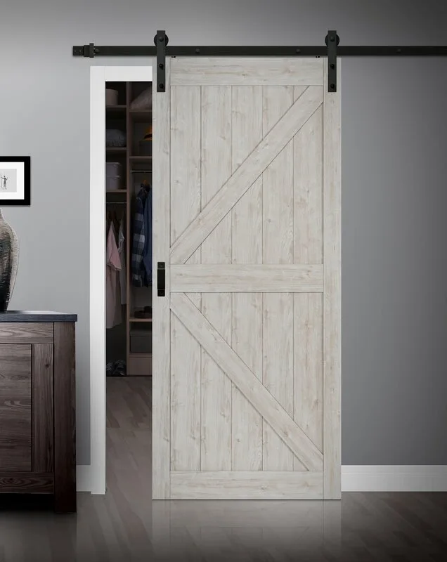 A whitewashed wooden sliding barn door with black metal hardware hangs on a dark grey wall next to a closet opening.