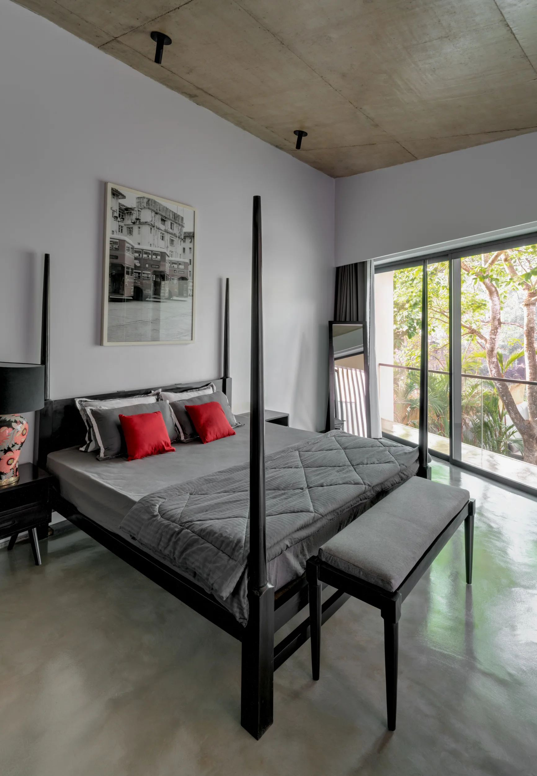 A modern bedroom featuring a black canopy bed, polished concrete flooring, exposed concrete ceiling, and large glass sliding doors.
