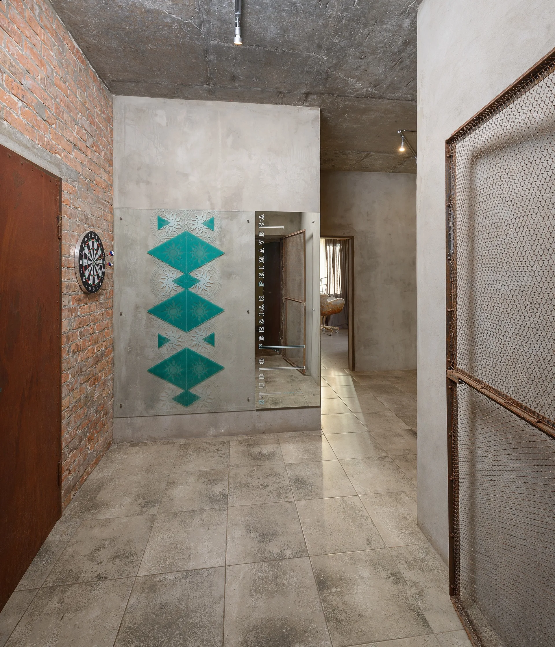 An industrial hallway with exposed brick, smooth concrete walls, a decorative glass panel, and large floor tiles.