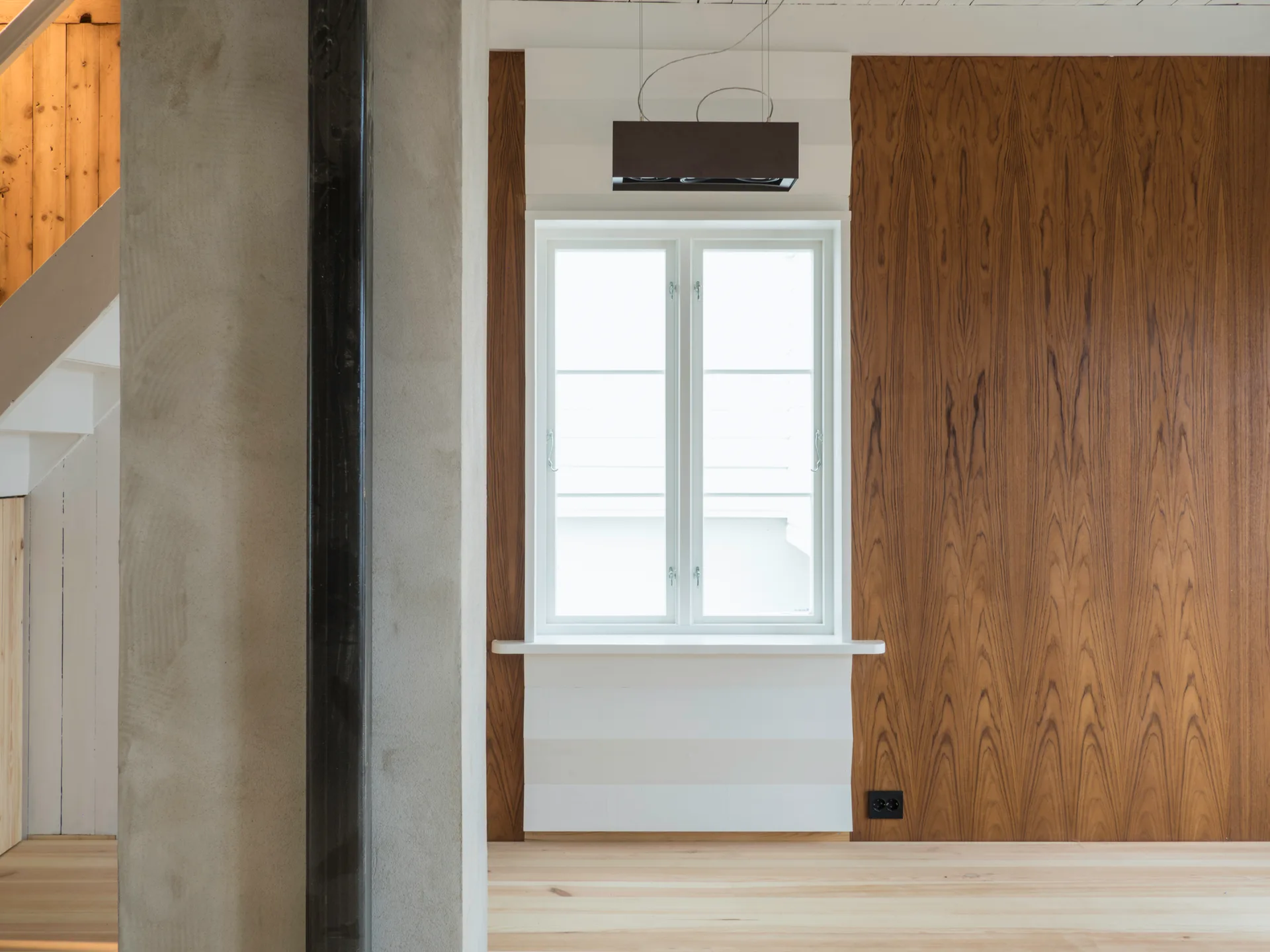 A white casement window is set in a white accent wall flanked by vertical wood paneling, with an exposed concrete column in the foreground.