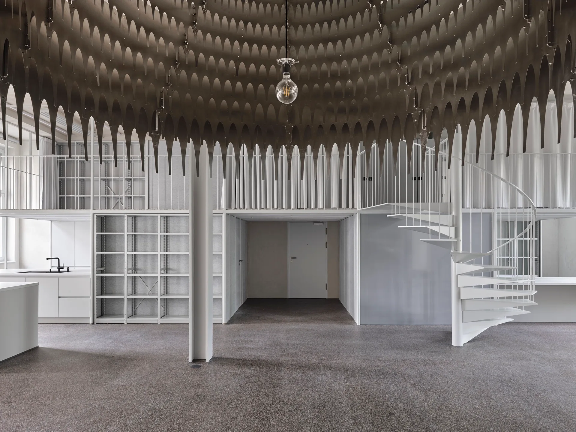 A minimalist industrial loft space featuring a white spiral staircase, open mezzanine level, and a large perforated metal dome ceiling fixture.